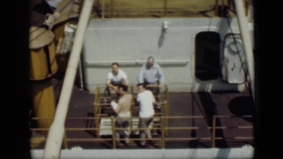 1946 Cairo 8mm footage showing four men in light clothing gathered on a boat deck beside yellow railings and cabin structures.