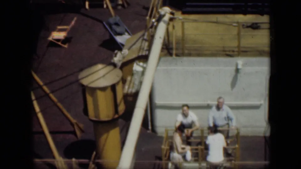 1946 Cairo home-movie frame with men gathered around deck chairs on a boat, near yellow railings and deck equipment.