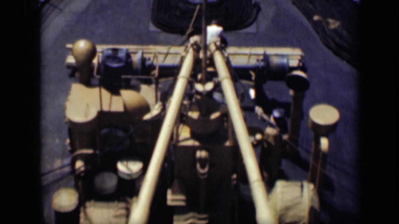 Rear ship deck with coiled rope, barrels, poles, and blue water behind.