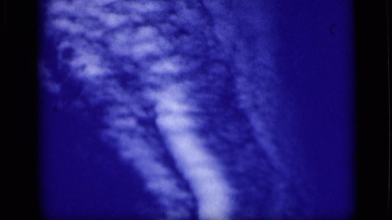 Deep blue frame with pale textured clouds or sky forms and visible film grain.