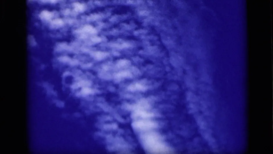 Blue-tinted 8mm footage shows cloudy sky texture with pale cloud bands and visible gate edge.