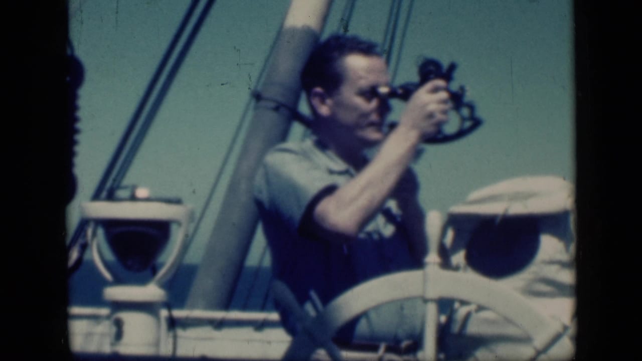 Man looks through a sextant with ship rigging and a white wheel in the foreground.