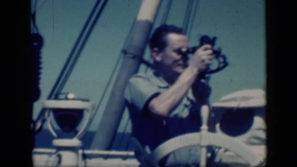 The final frame keeps the man, sextant, white ship wheel, mast, and rigging in view, with soft 8mm focus and blue sky behind.