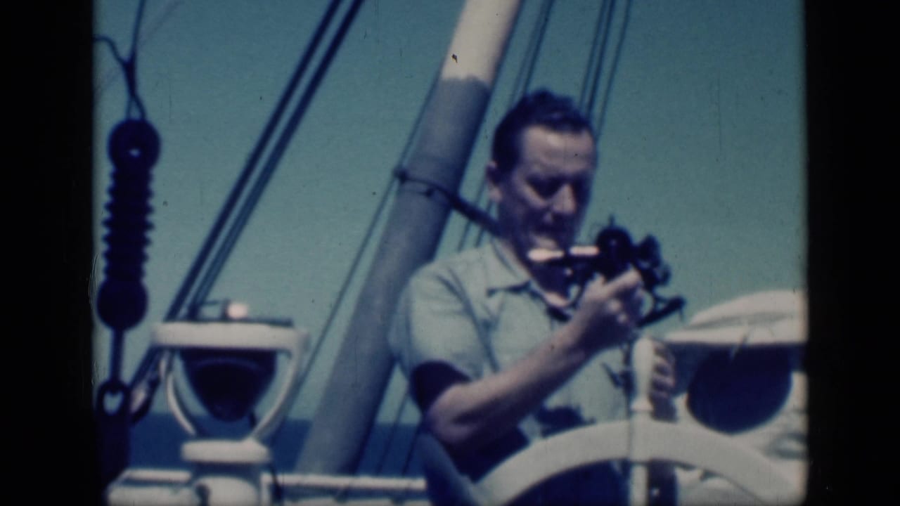 Man looking down at a cine camera near sailboat rigging and a white wheel.