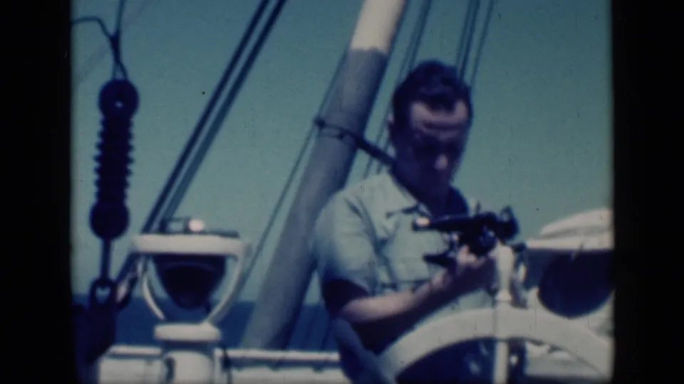 A man on a Cairo sailboat in 1946 lowers his cine camera, framed by a mast, rigging, deck hardware, and bright sky.