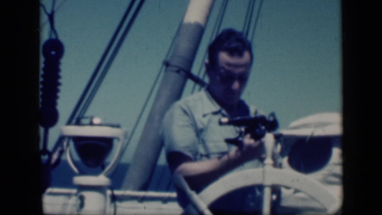 1946 Cairo travel footage frame showing a man on a ship deck preparing a sextant beside a wheel and rigging.