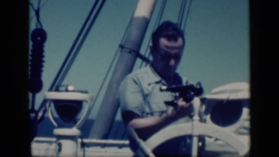 1946 Cairo travel footage frame showing a man on a ship deck preparing a sextant beside a wheel and rigging.