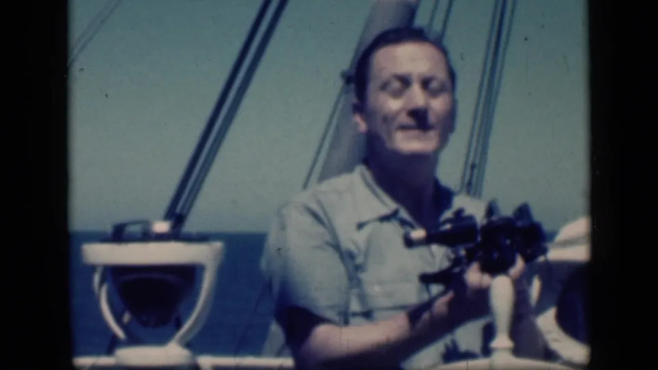 In the 1946 Egypt home-movie clip, the man smiles toward the camera while holding binoculars on deck.