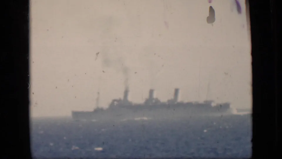 A distant ship sits on the horizon in faded 8mm footage, with open water below and pale sky above.