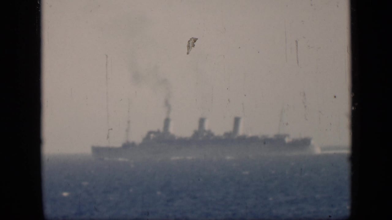 Large steamship seen beyond open water, framed by dark 8mm film borders.
