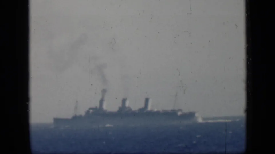 Soft 8mm frame of a distant steamship at sea, with smoke from its funnels and a low horizon line.
