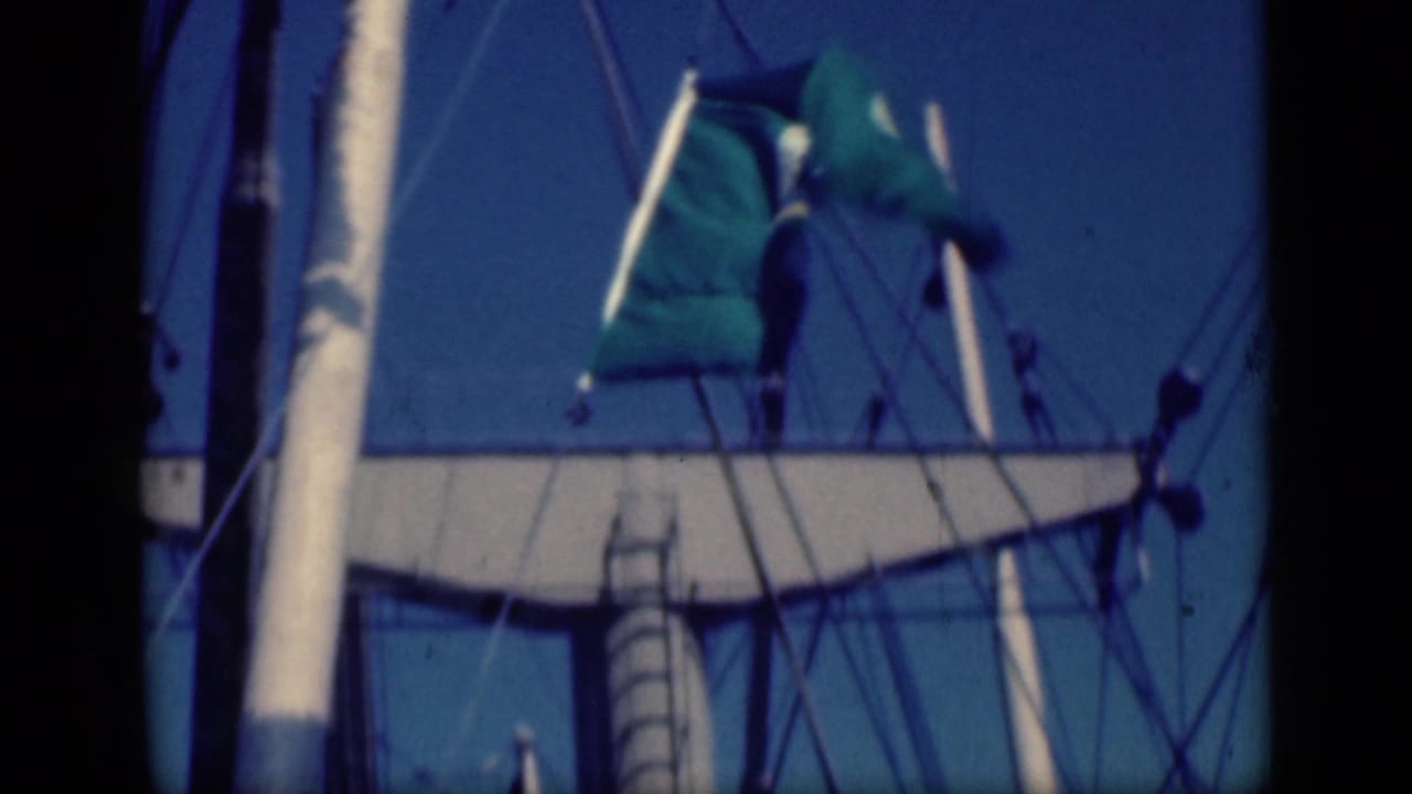 1946 Cairo home-movie frame showing a green crescent-and-star flag near a sailboat mast and rigging under blue sky.