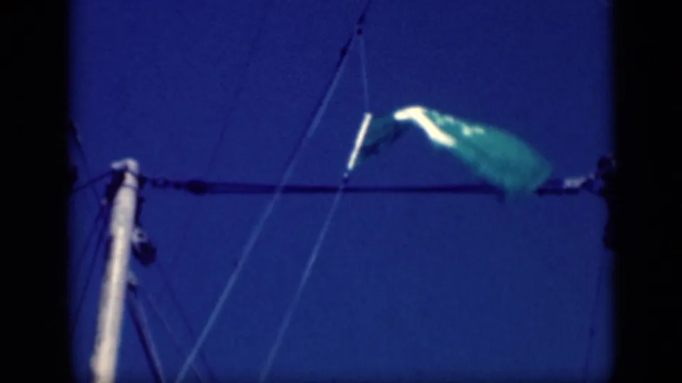 1946 Cairo home-movie frame with a windblown green flag, pale mast, and diagonal sailboat rigging against blue sky.