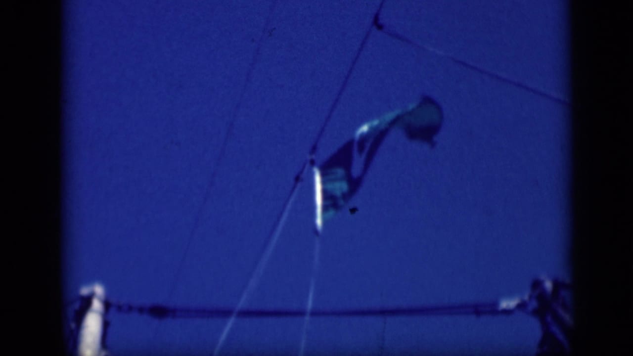 1946 8mm frame showing a United States flag on ship rigging against a deep blue sky, with dark film borders visible.