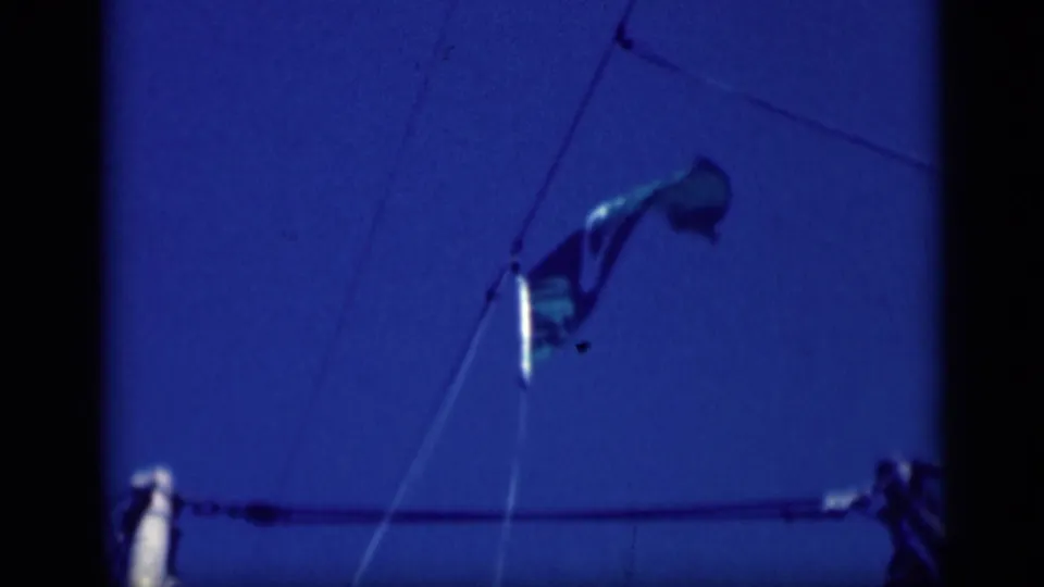 1946 8mm frame showing a United States flag on ship rigging against a deep blue sky, with dark film borders visible.