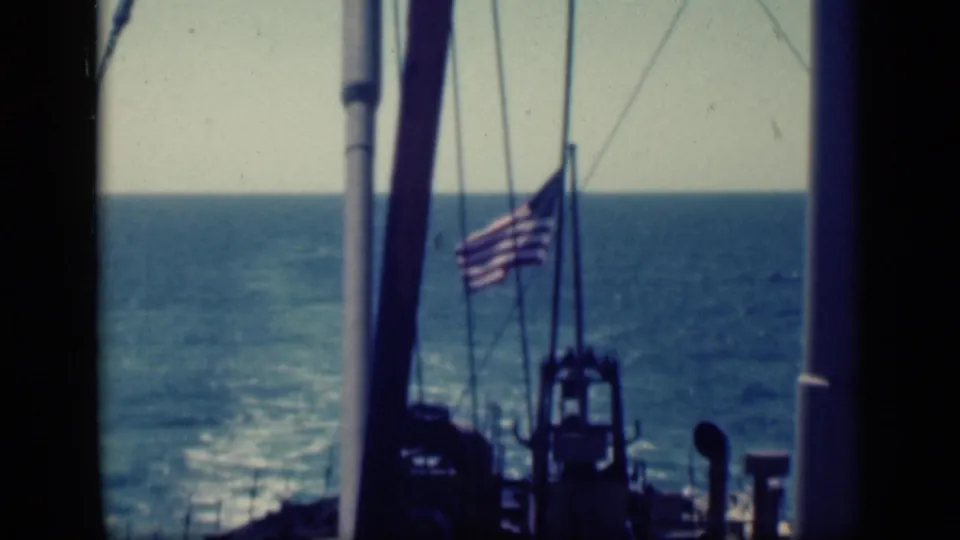1946 8mm frame showing the ship stern area, United States flag, mast, rigging, and open ocean horizon.