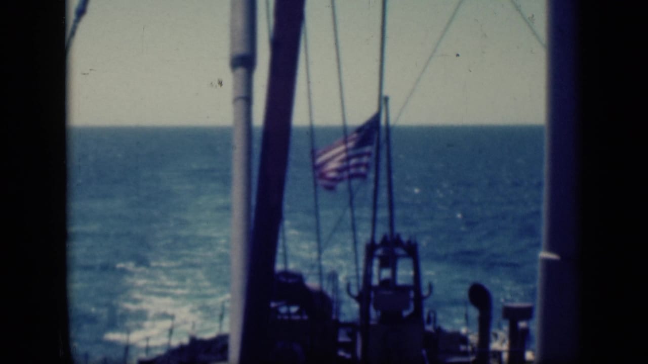 American flag and ship rigging in front of blue ocean and horizon.