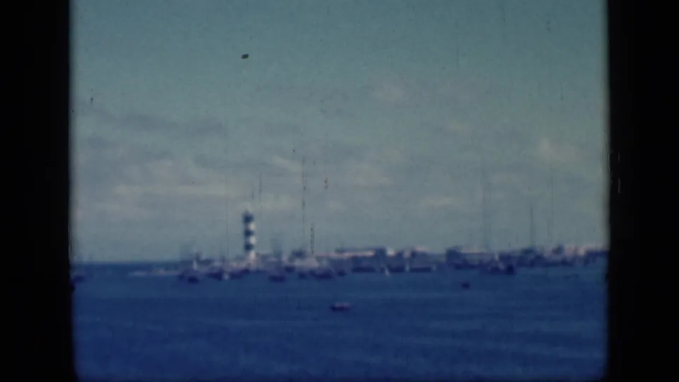 Distant harbor shoreline appears across the water in this 1946 Egypt travel frame, with a tower or lighthouse and low structures visible.