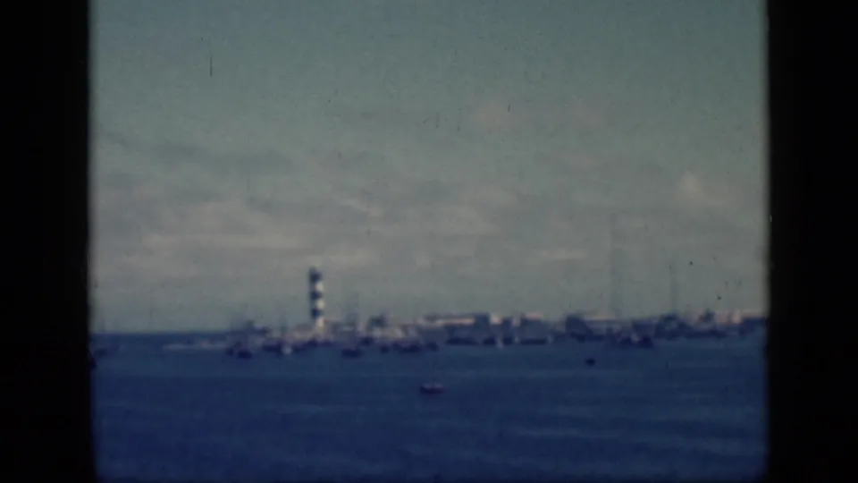 Final 1946 Egypt 8mm frame holding on a distant shoreline lighthouse, boats, blue water, and cloudy sky.
