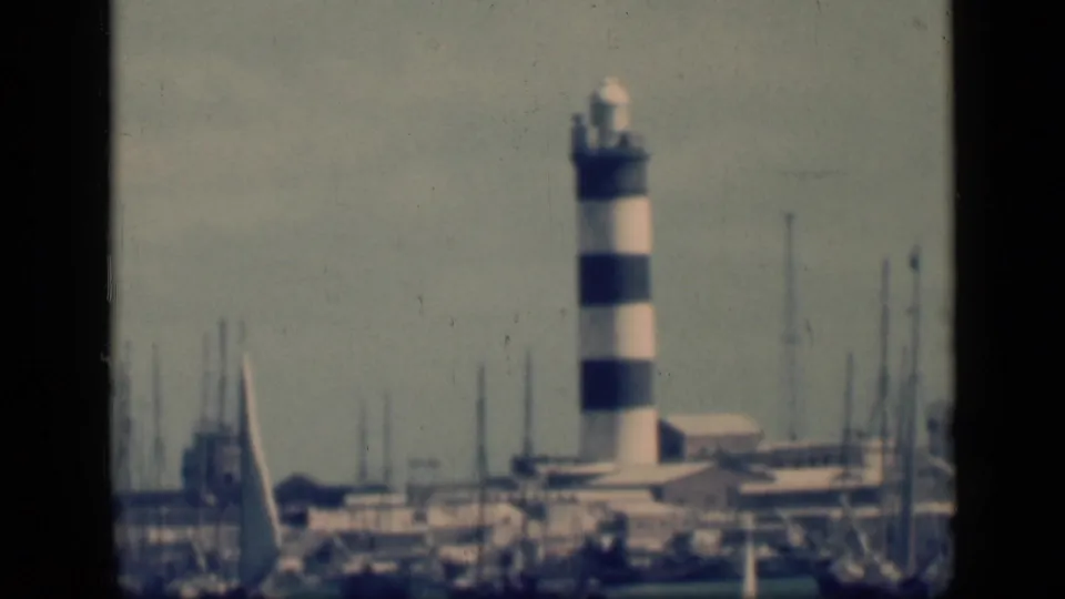 1946 Egypt 8mm frame with a black-and-white striped lighthouse rising above marina masts, boats and low waterfront structures.
