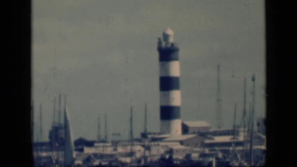 1946 Egypt 8mm frame centering the striped lighthouse behind marina masts, boats and low harbor buildings in a hazy waterfront scene.