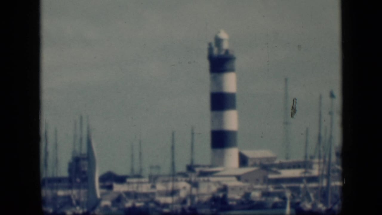 Harbor light tower framed by marina masts and a pale sky.