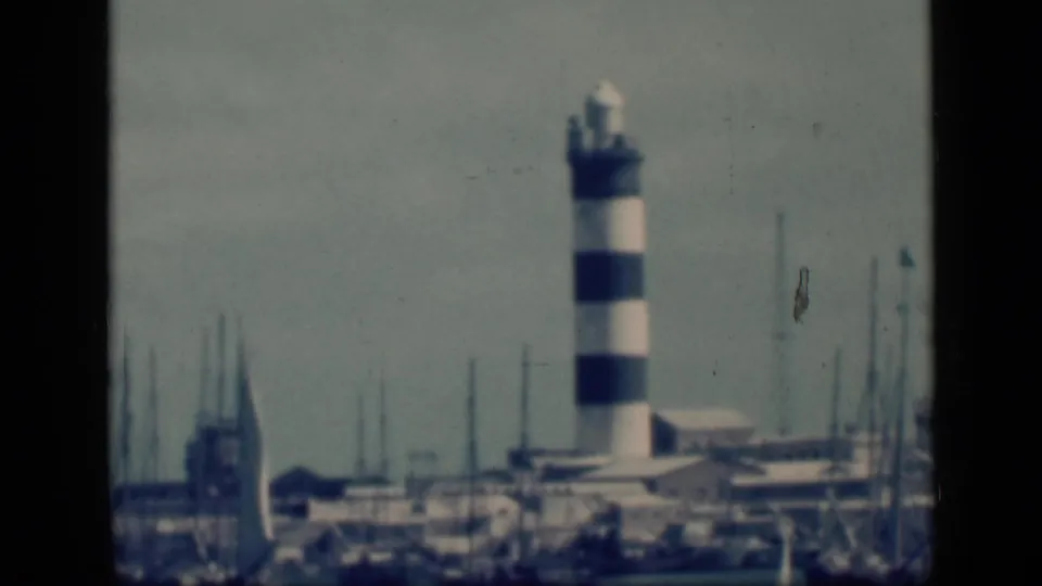 A distant striped harbor light stands near clustered boat masts in 1946 Cairo, Egypt, filmed on soft color 8mm stock.
