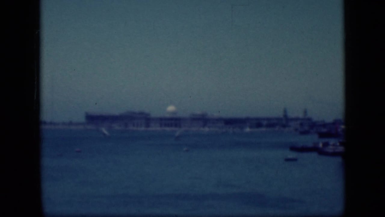 1940s Egypt home-movie frame showing a distant waterfront building, calm water, small boats, and heavy black gate edges.