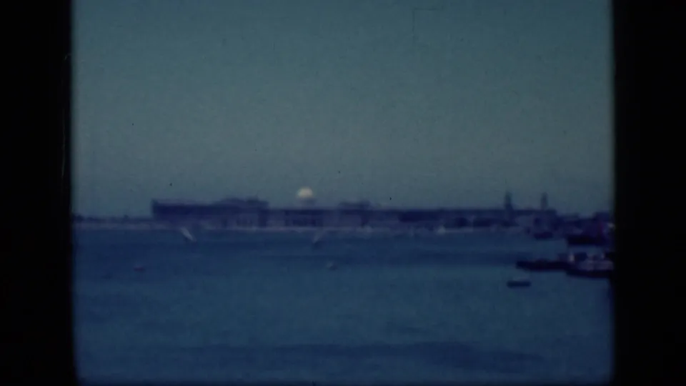 1940s Egypt home-movie frame showing a distant waterfront building, calm water, small boats, and heavy black gate edges.