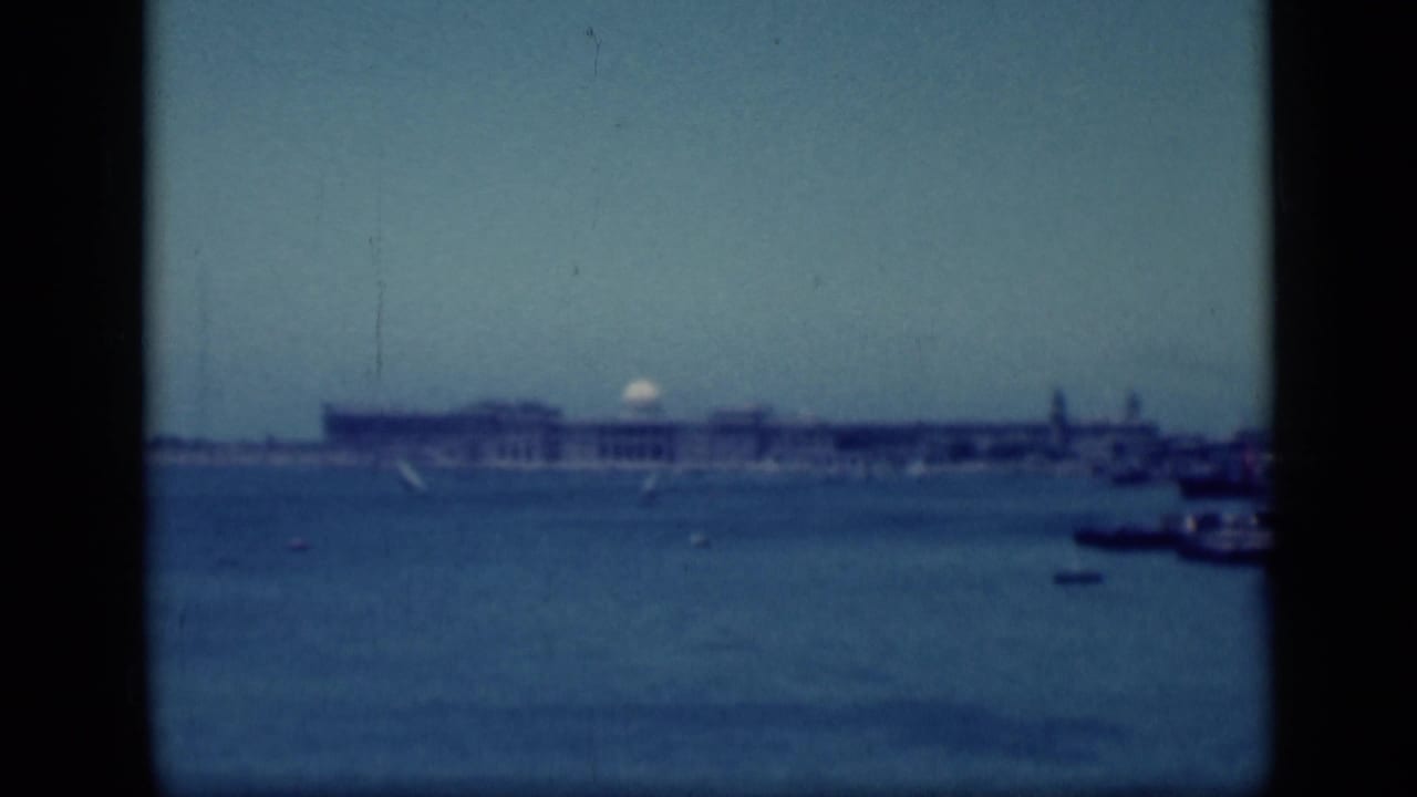 Wide waterfront view with distant buildings, boats, and a tower shape.