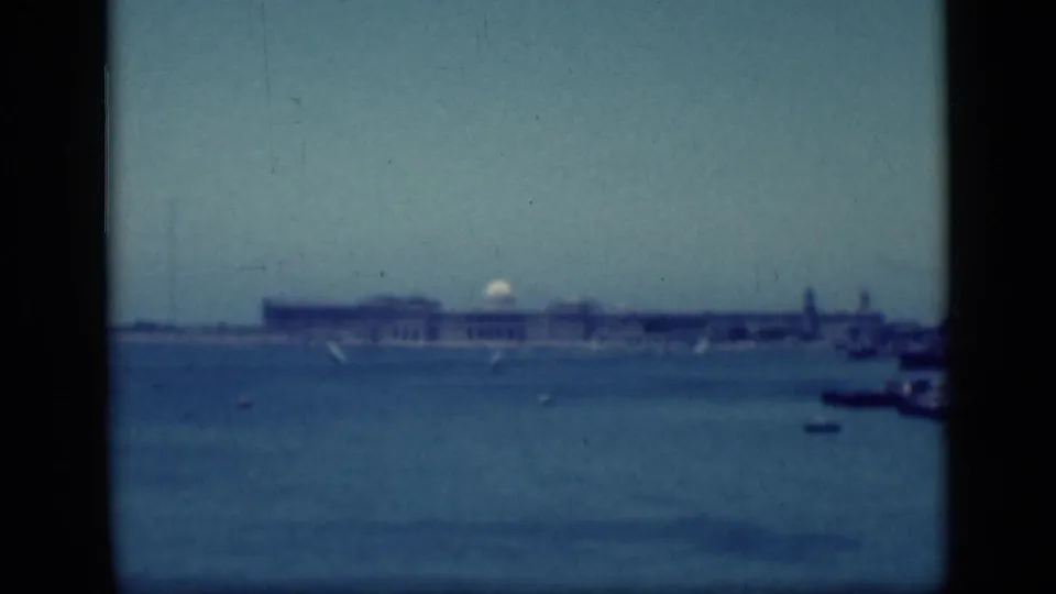 1940s Egypt home-movie still showing a distant pale building complex across water with small boats and dark frame borders.