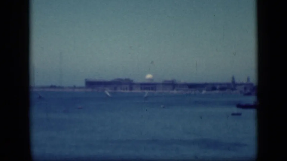 1940s Egypt waterfront view with a far building complex, calm blue water, small boats, and visible 8mm gate edges.