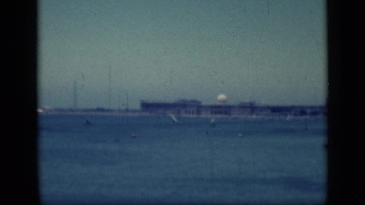 Hazy waterfront view with a pale building, small boats, and dark central framing.