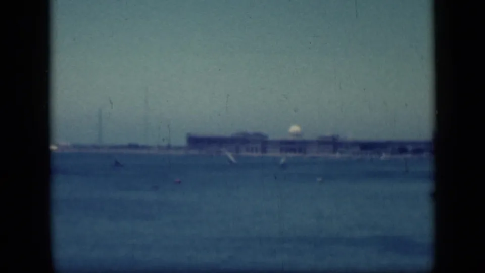 1946 Cairo, Egypt, travel footage frames a pale waterfront structure across the water with small sailboats and shoreline haze.