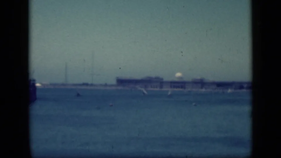 Wide 1946 home-movie frame from Cairo, Egypt, showing blue water, sailboats, and a distant pale waterfront building.