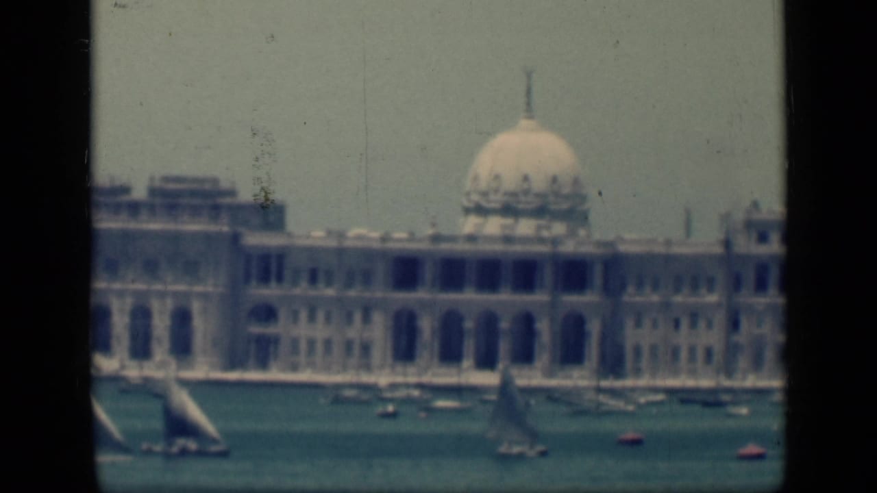 1946 Egypt home-movie frame of a large domed building across harbor water, with sails and small craft in front.