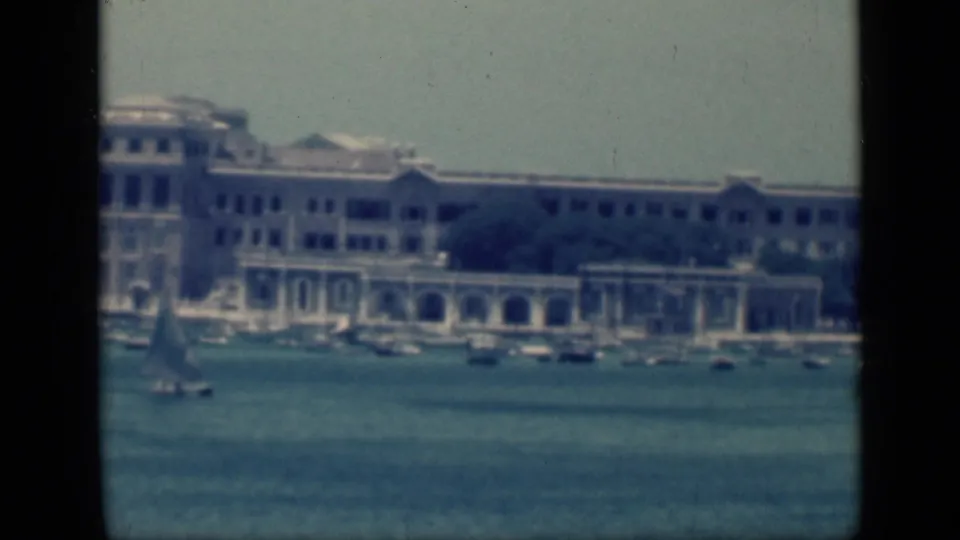 1946 Egypt 8mm frame showing a waterfront building with arches, tree cover, and small boats on the harbor.