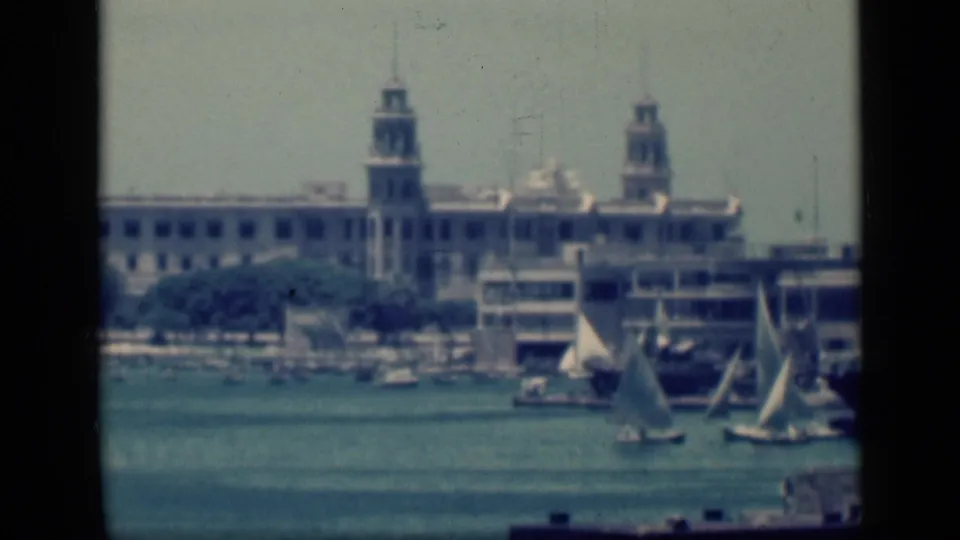 1946 Cairo harbor view with white sailboats on blue water and pale waterfront architecture with twin tower-like structures beyond.