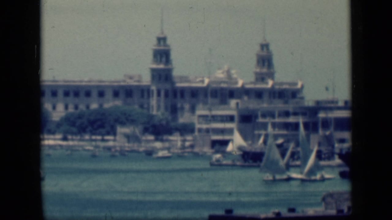 1946 Cairo, Egypt home-movie frame showing sailboats crossing calm water before a large waterfront building with twin towers.