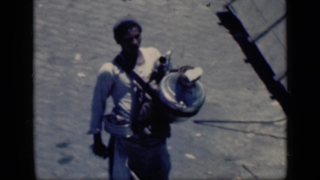 In 1946 Cairo home-movie footage, a young man in a light shirt walks over dusty ground carrying a large round object.