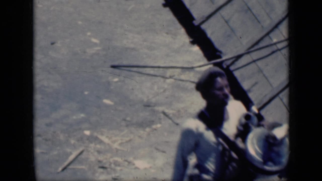 Young man partly framed at right, carrying a round object near shadowed structures.