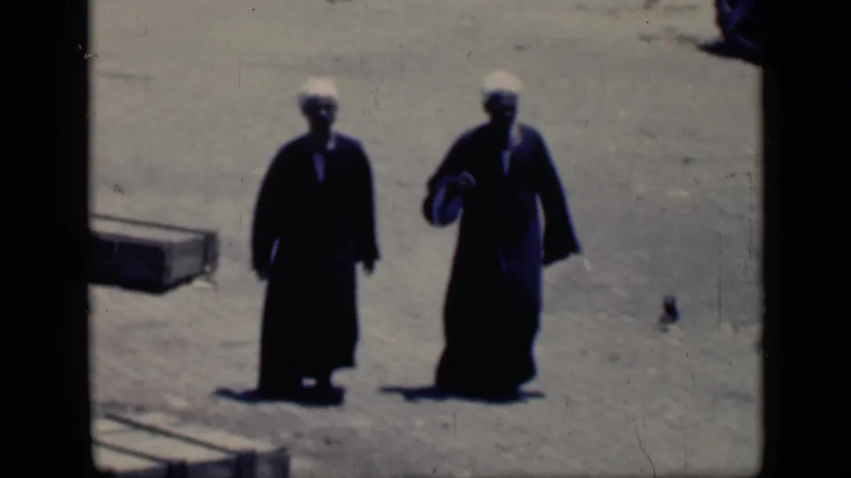 The 1946 Cairo frame shows two men in dark robes and white head coverings on bright dusty ground, one holding a small item.