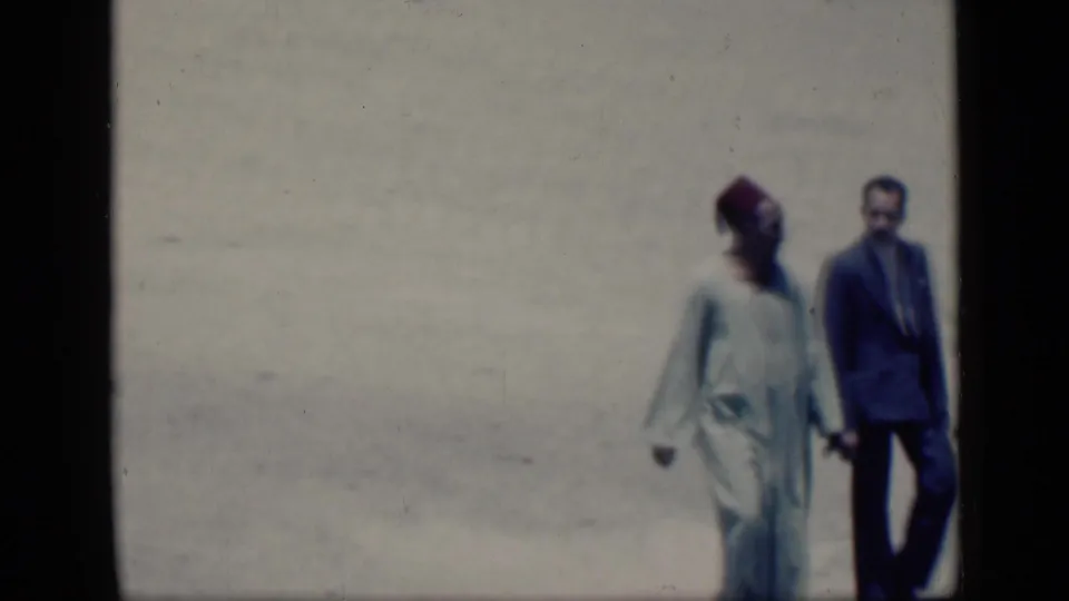 The Cairo frame shows a man in a pale robe and red fez walking hand in hand with a suited man near the right edge of the shot.