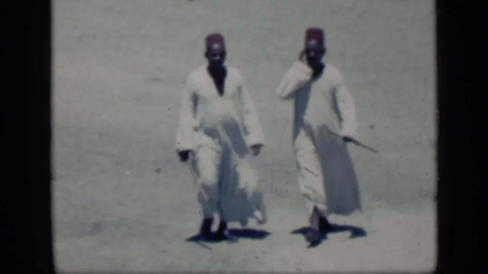 Two men in white robes and red fez-style hats walk toward the camera in the 1946 Cairo home-movie footage.