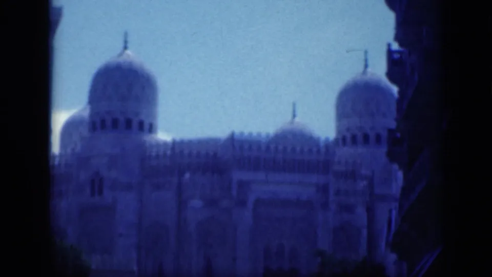 1946 Cairo 8mm frame emphasizing the domes and upper facade of a large Islamic landmark against blue sky.