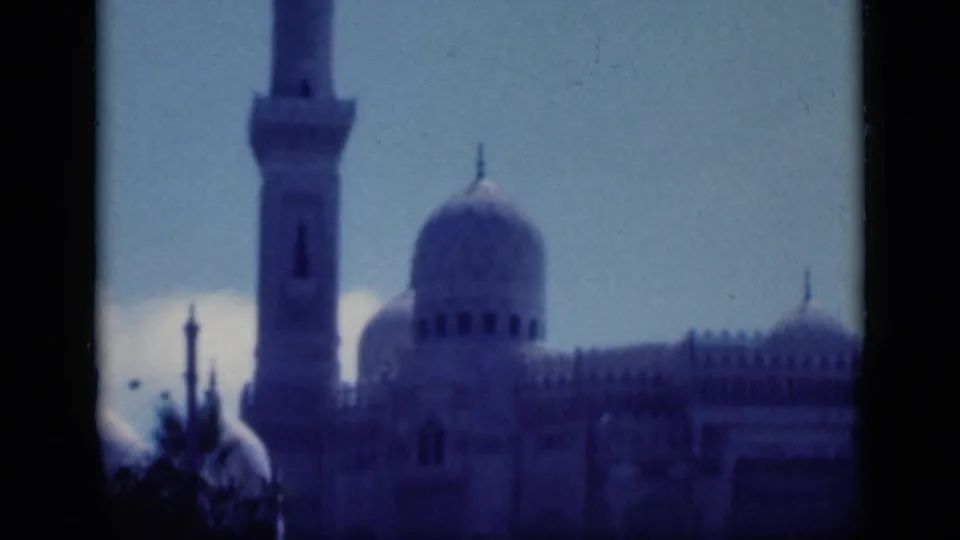 1946 Cairo home-movie frame showing a minaret, large dome, and mosque facade under bright sky with deep blue film cast.