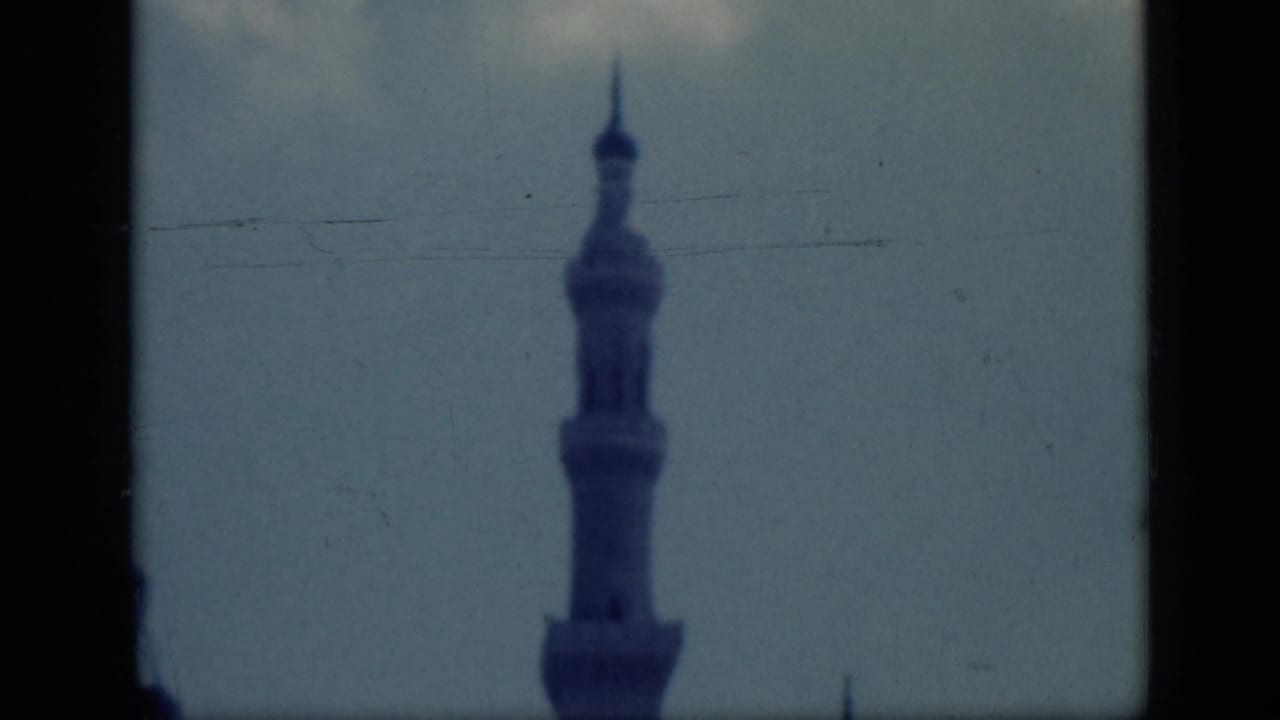 Minaret centered against pale sky with scratches and dark frame edges.