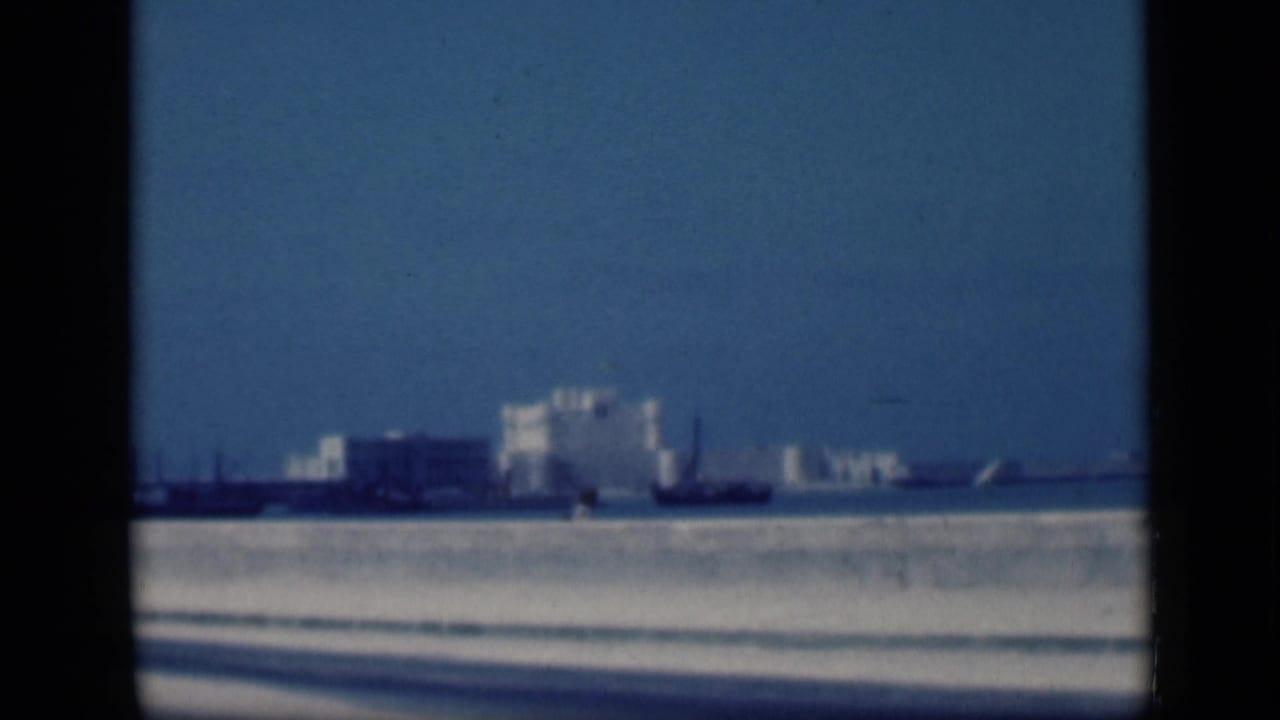 Distant pale buildings across a bright open landscape under a clear blue sky.