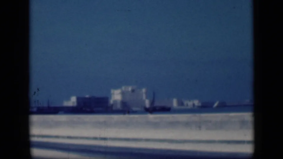 1946 Cairo 8mm frame showing a hazy distant skyline, dark foreground structures, and pale buildings under blue sky.