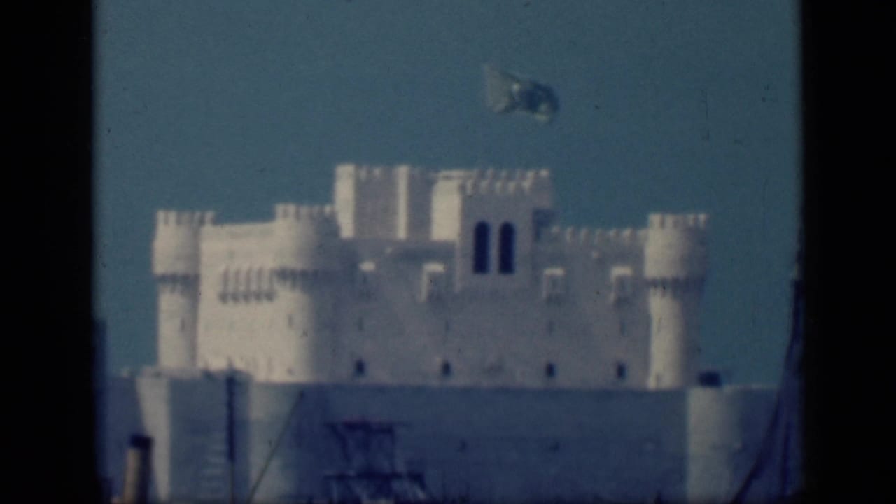 1946 Cairo frame with a white fortified-looking facade, round towers, dark arched openings, and a blue flag in the sky.